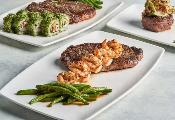 Plates of steak, shrimp, green beans, and sushi on a table.
