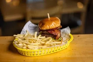 Double burger, bacon, lettuce, and fries in a yellow basket.