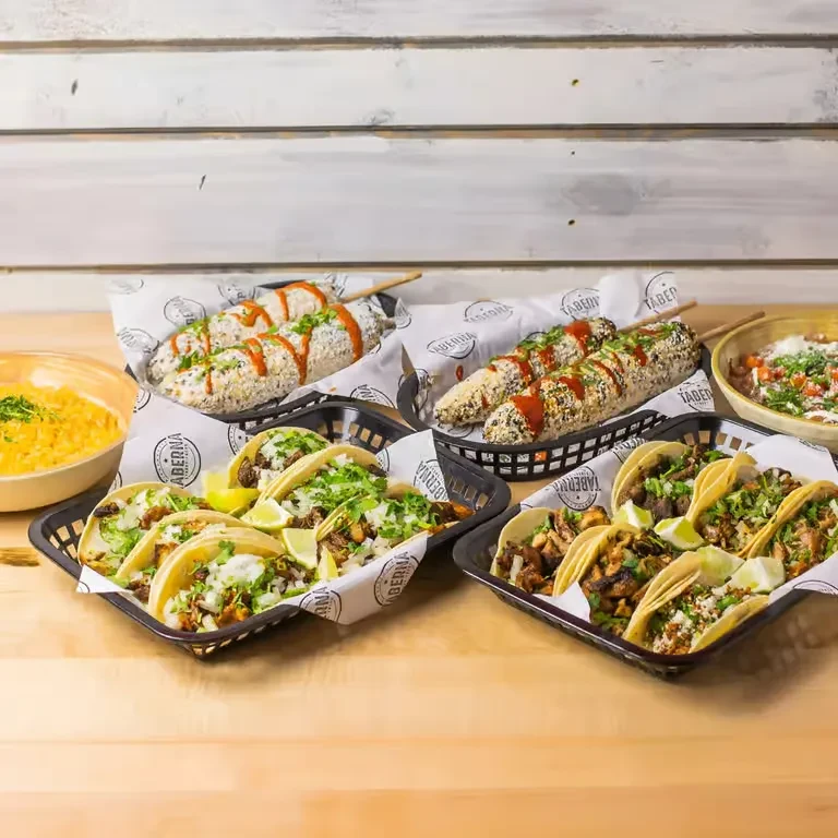 Mexican tacos, elote, rice, and beans on a wood table.