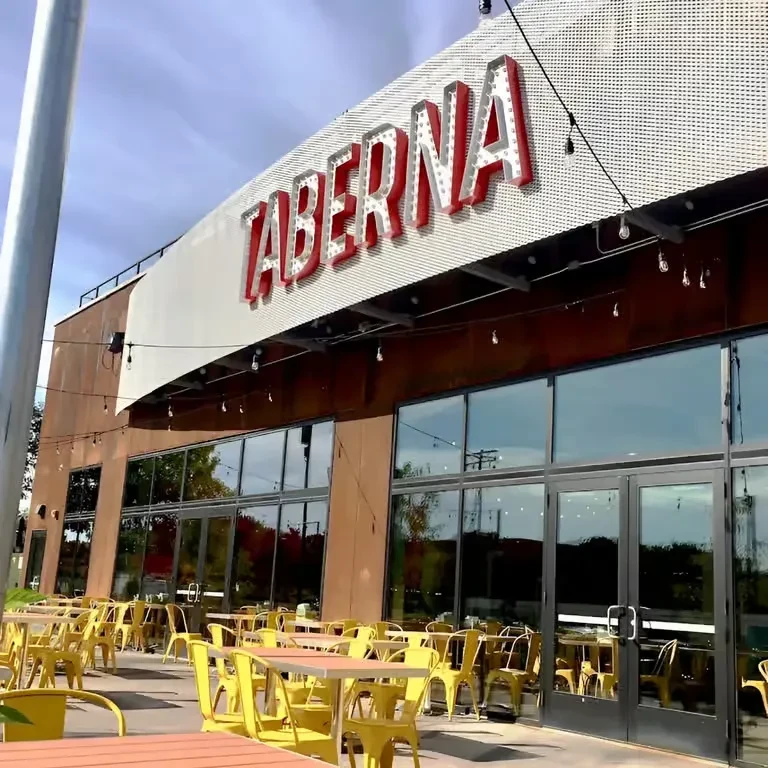 Sunny exterior of TABERNA restaurant with empty patio tables and chairs.