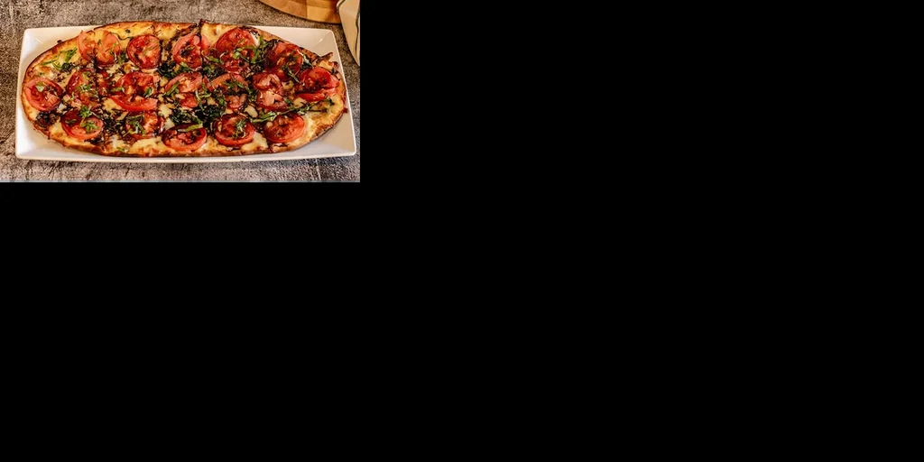 Rectangular flatbread with bright tomatoes, green herbs, and dark glaze.