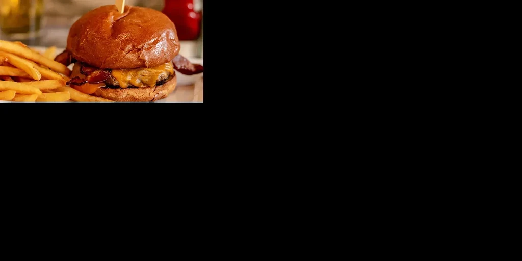 Close-up cheeseburger with bacon, melted cheese, and golden french fries.