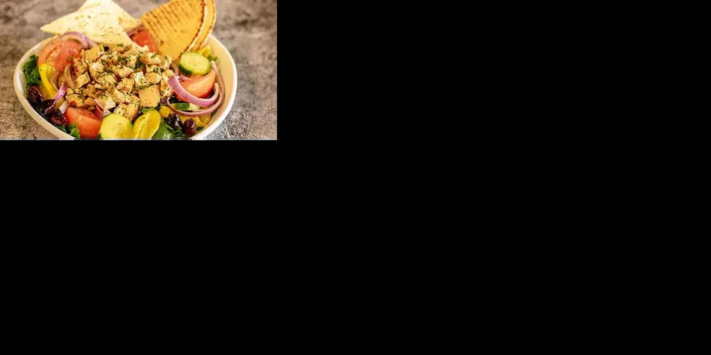 Grilled chicken salad, vegetables, pita bread, in white bowl on stone.