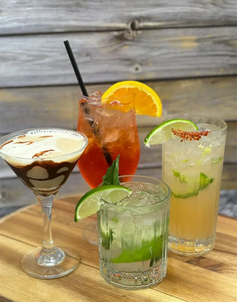 Four distinct cocktails on a wooden surface, with a rustic wall.