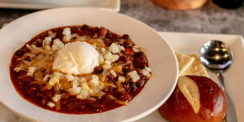 Bowl of chili with melted cheese, sour cream, onions, and crackers.