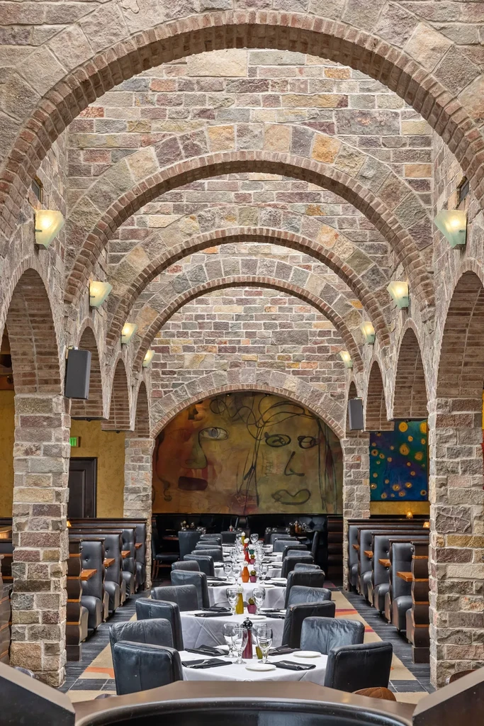 Stone arch restaurant interior with set dining tables and abstract art.