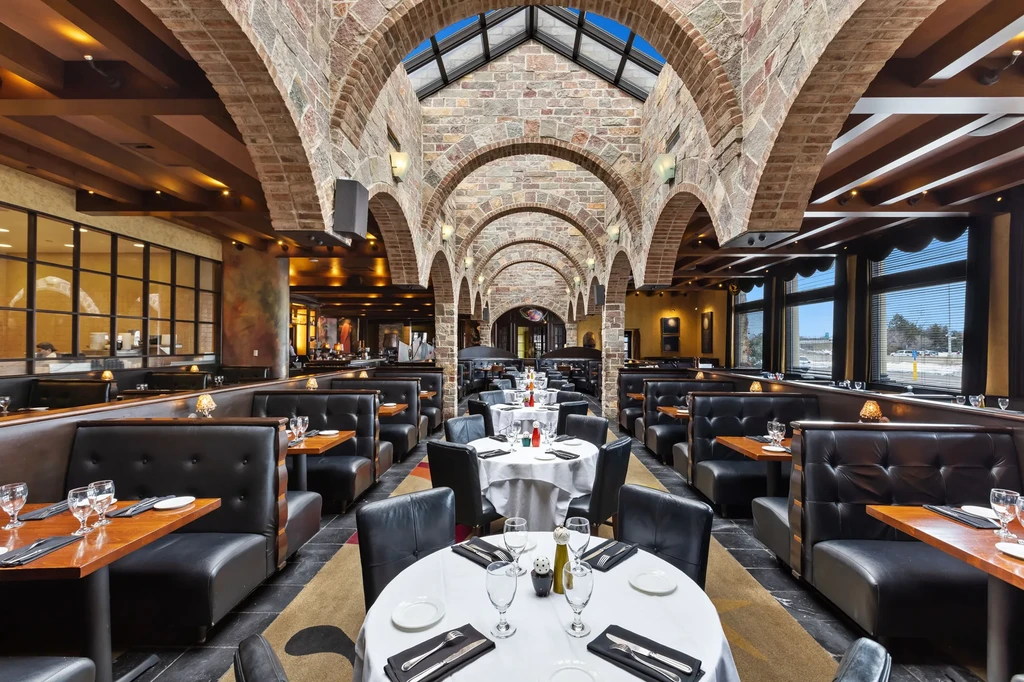 Upscale restaurant interior with vaulted stone arches, skylight, set tables.