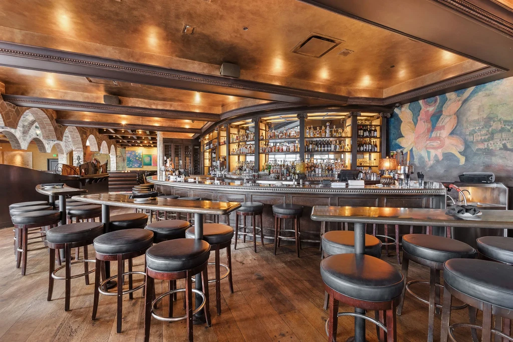 Upscale empty bar with dark wood, backlit liquor, and a metallic ceiling.