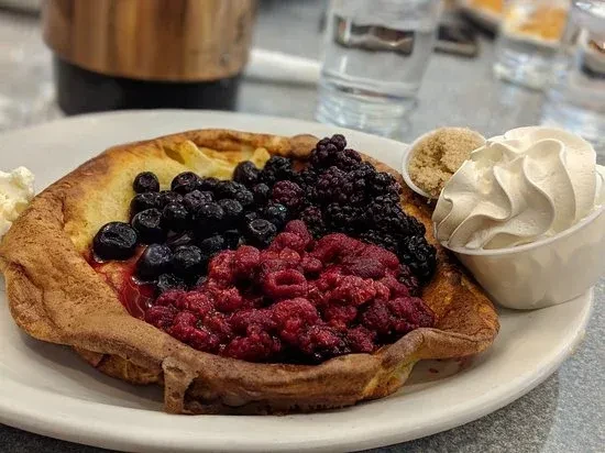 Fluffy pancake topped with mixed berries, cream, brown sugar, and whipped cream.