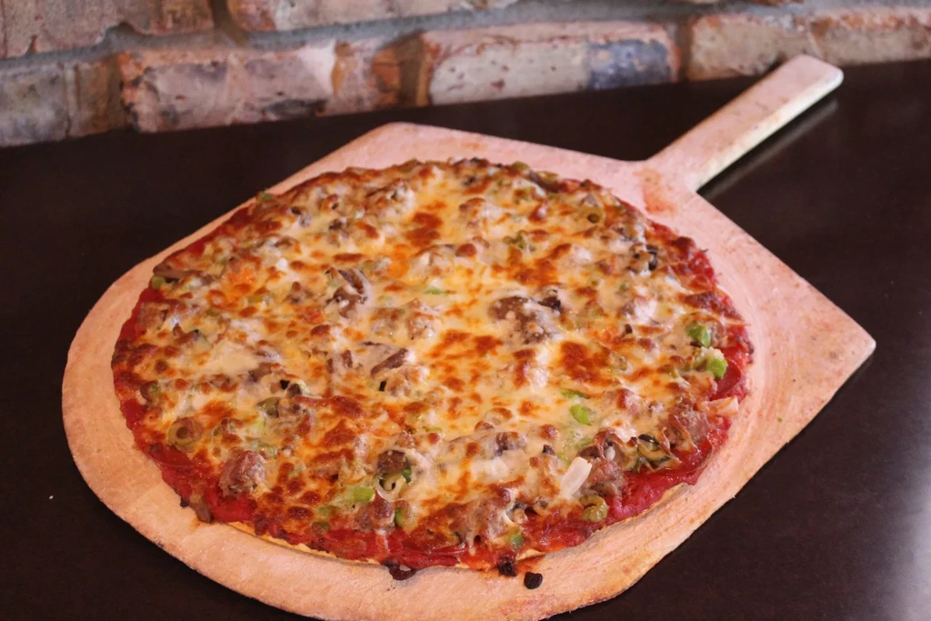 Hot, cheesy pizza with sausage, green peppers on a wooden peel.