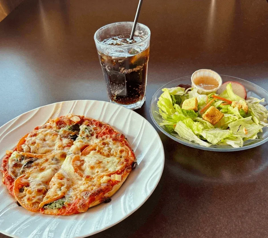 A personal pizza, green salad, and dark soda on a tabletop.