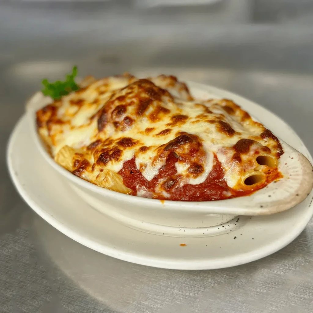 Baked pasta with red sauce, bubbling golden cheese, and green herb.