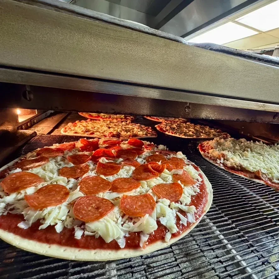 Multiple pizzas, raw and cooking, inside a commercial conveyor oven.