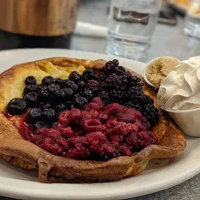 A large baked pancake with fresh berries, whipped cream, and brown sugar.