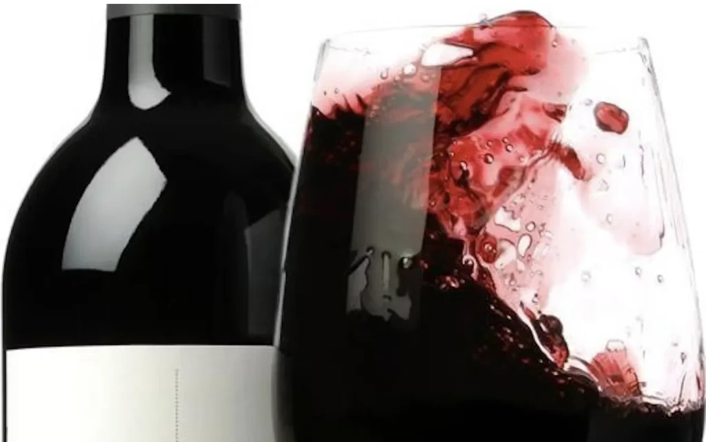 Dark wine bottle and glass with red wine splashing on white.