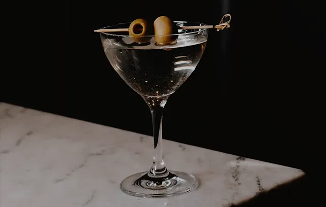 Clear martini with two olives on a skewer, dark background, marble.