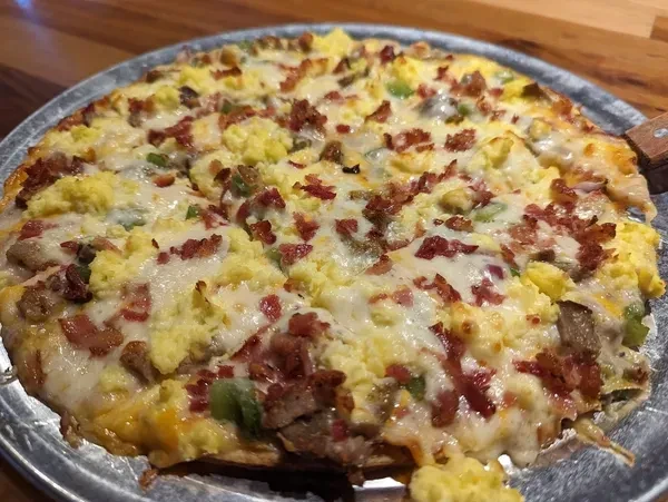 Large breakfast pizza with eggs, bacon, and melted cheese on a pan.