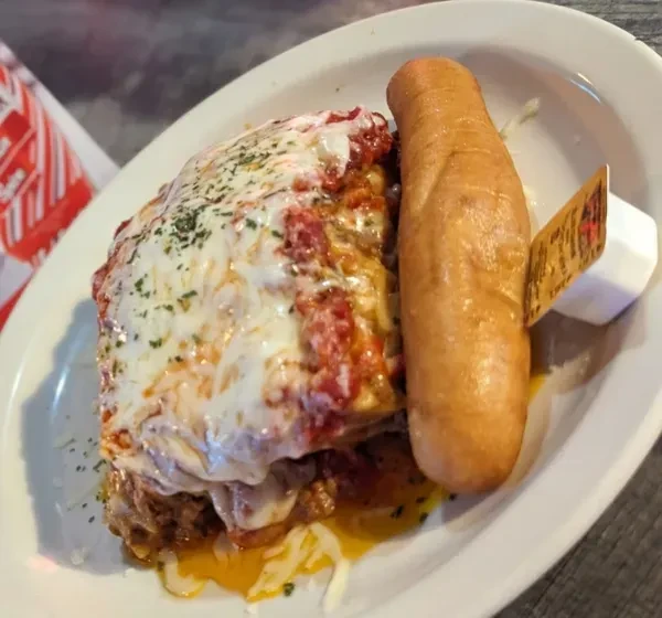 Baked pasta with melted cheese, tomato sauce, herbs, and breadstick.