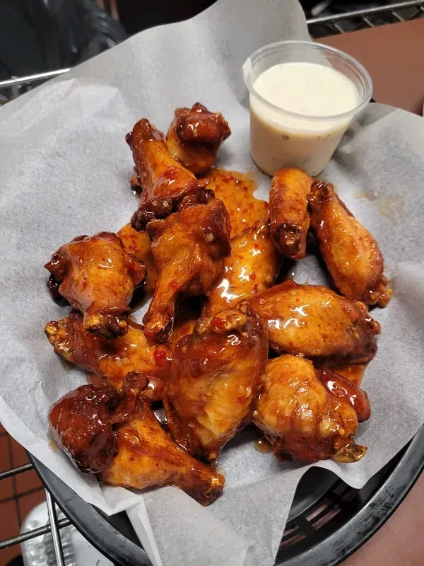 Glossy spicy chicken wings in a dark basket with creamy dipping sauce.