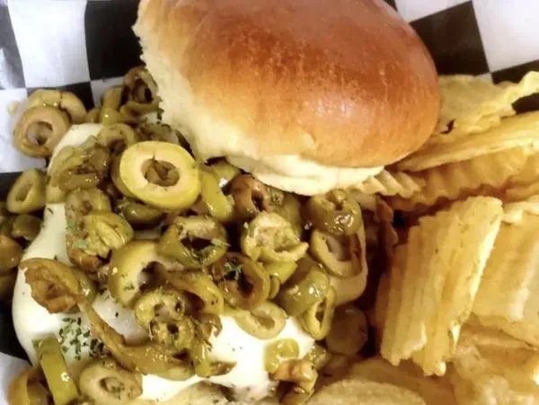 Overhead burger with melted cheese, green olives, and ruffled chips.
