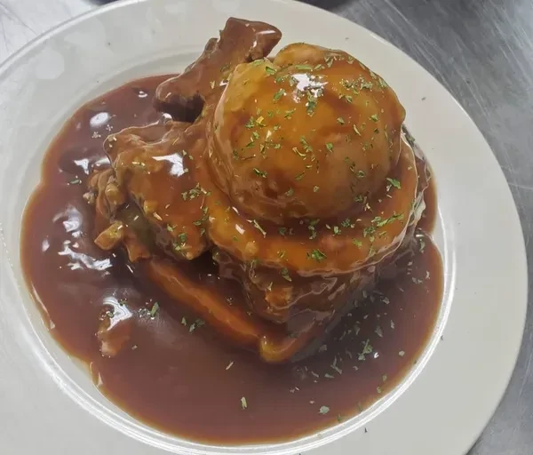 Plated meat and mashed potatoes, drenched in brown gravy with green herbs.