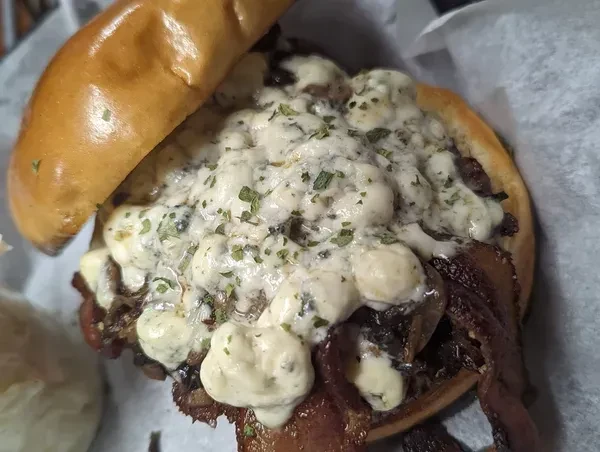 Overhead close-up of gourmet burger with blue cheese, herbs, and dark filling.