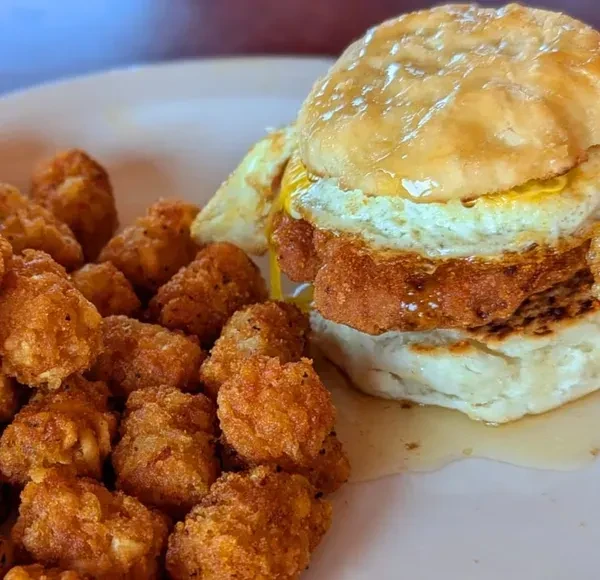 Close-up: Chicken biscuit sandwich, fried egg, syrup, and tater tots.