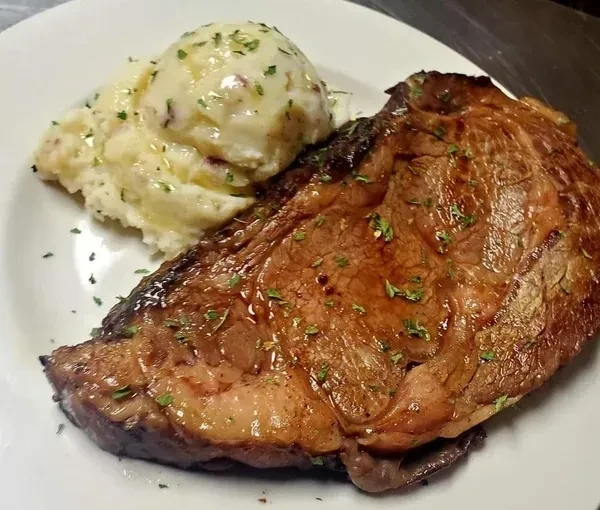 Well-browned steak, mashed potatoes, and herbs on a white plate.