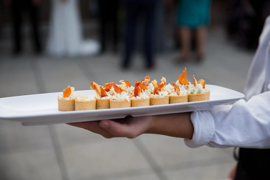 Hand holding platter of ten canapés with cured meat and herbs.