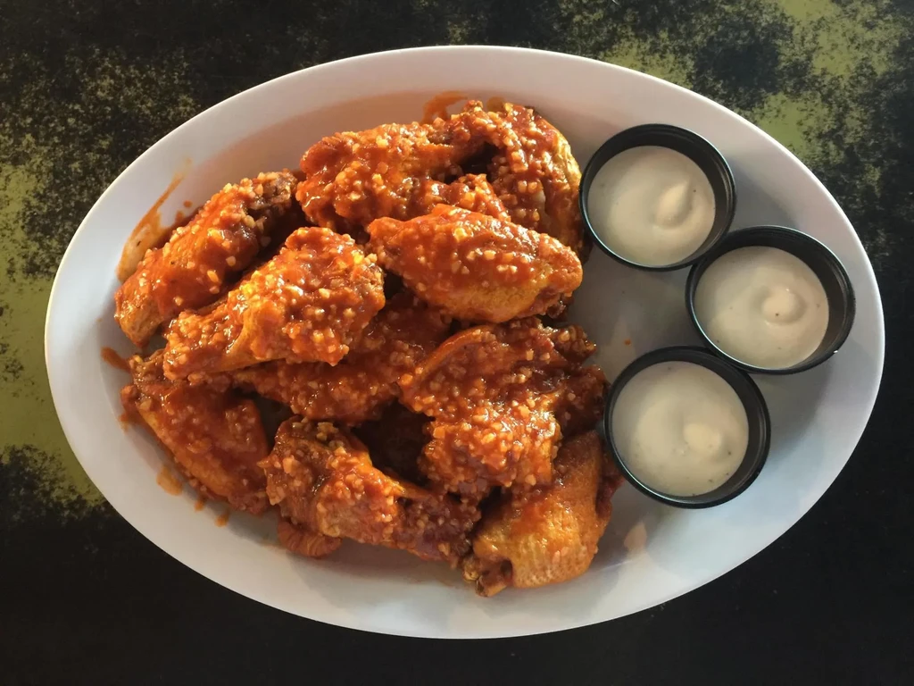 White oval platter of saucy orange-red wings with three dipping sauces.