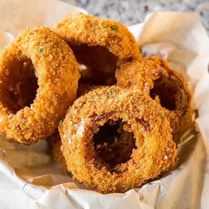 Crispy, golden-brown onion rings with green seasoning in a paper-lined basket.