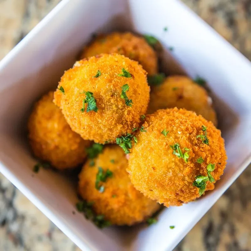 Crispy golden-brown fried spheres piled in a white bowl with herbs.