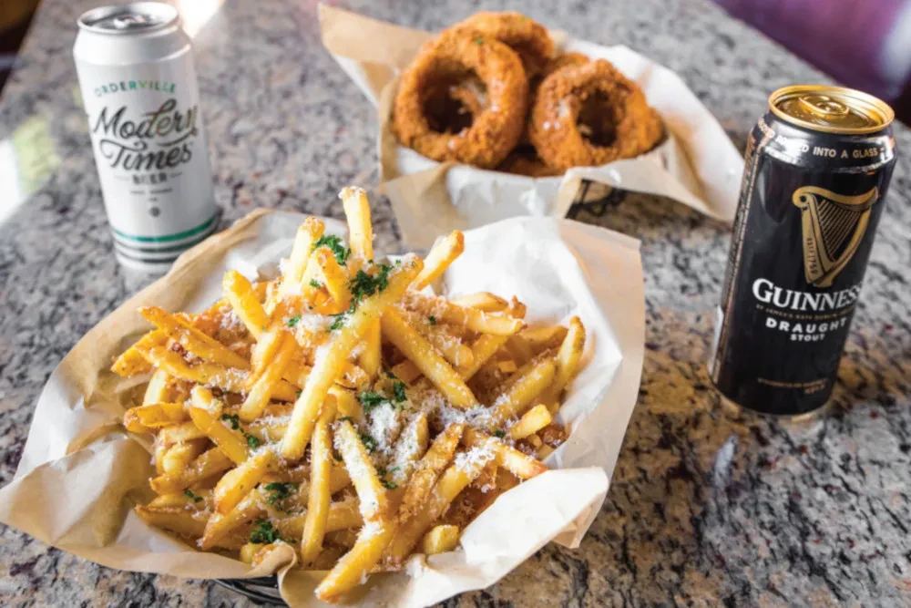 Fries, onion rings, Modern Times, and Guinness beer cans on counter.