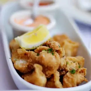 Close-up of crispy fried food, lemon wedge, herbs, and dipping sauce.