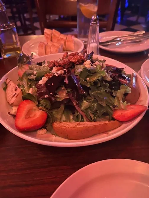 A colorful salad with lettuce, nuts, cheese, strawberries, and pears.