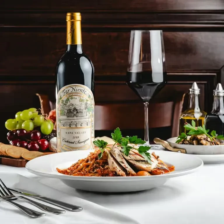 Pasta, chicken, Far Niente Cabernet, cheese, and grapes on an elegant table.