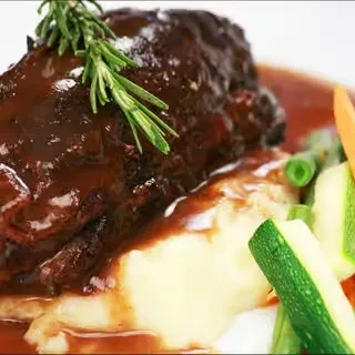 Plated braised short rib, mashed potatoes, zucchini, carrots, and rosemary.