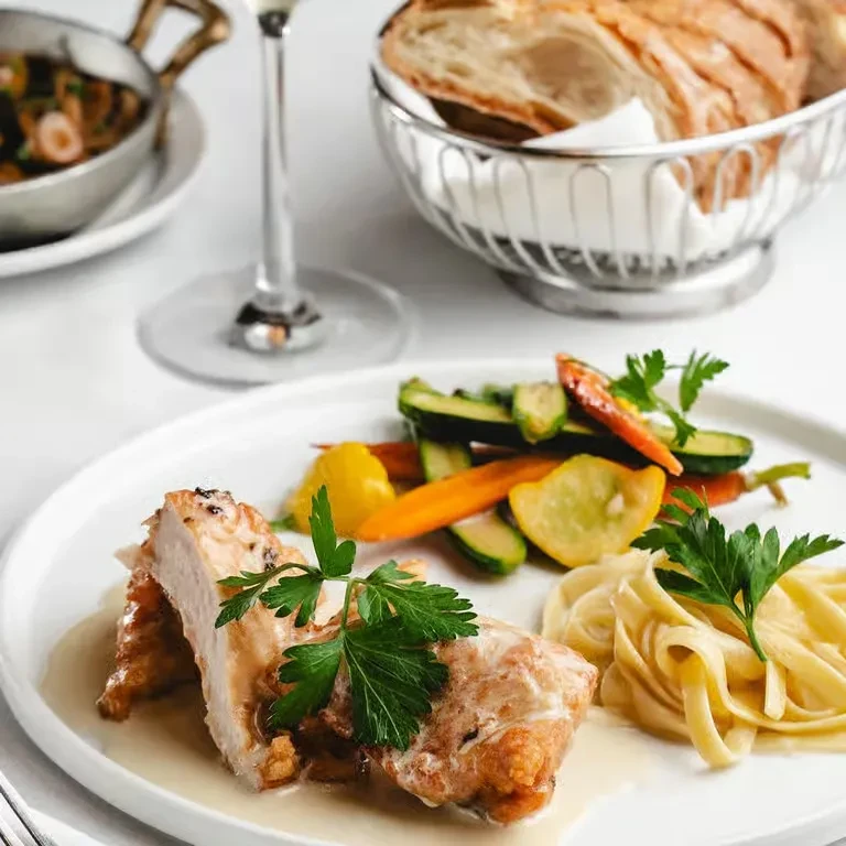 Plated chicken, tagliatelle, and colorful vegetables in an elegant restaurant.