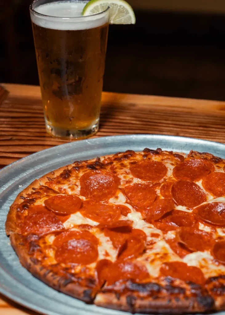 Pepperoni pizza and a glass of beer on a rustic wooden table.