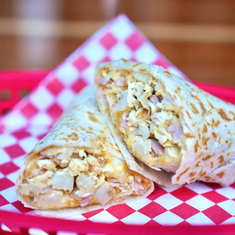 Breakfast burrito cut in half, showing eggs, potatoes, and melted cheese.