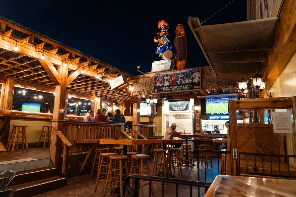 Patrons enjoy a lively wooden sports bar with string lights and TVs.