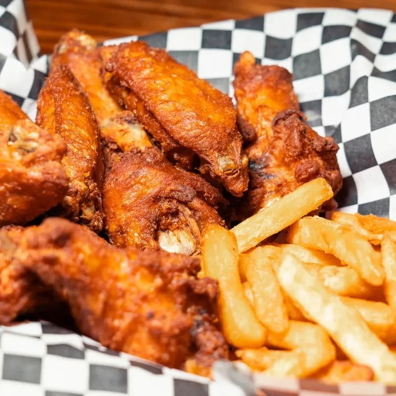 Crispy fried chicken wings and fries in a checkerboard basket.