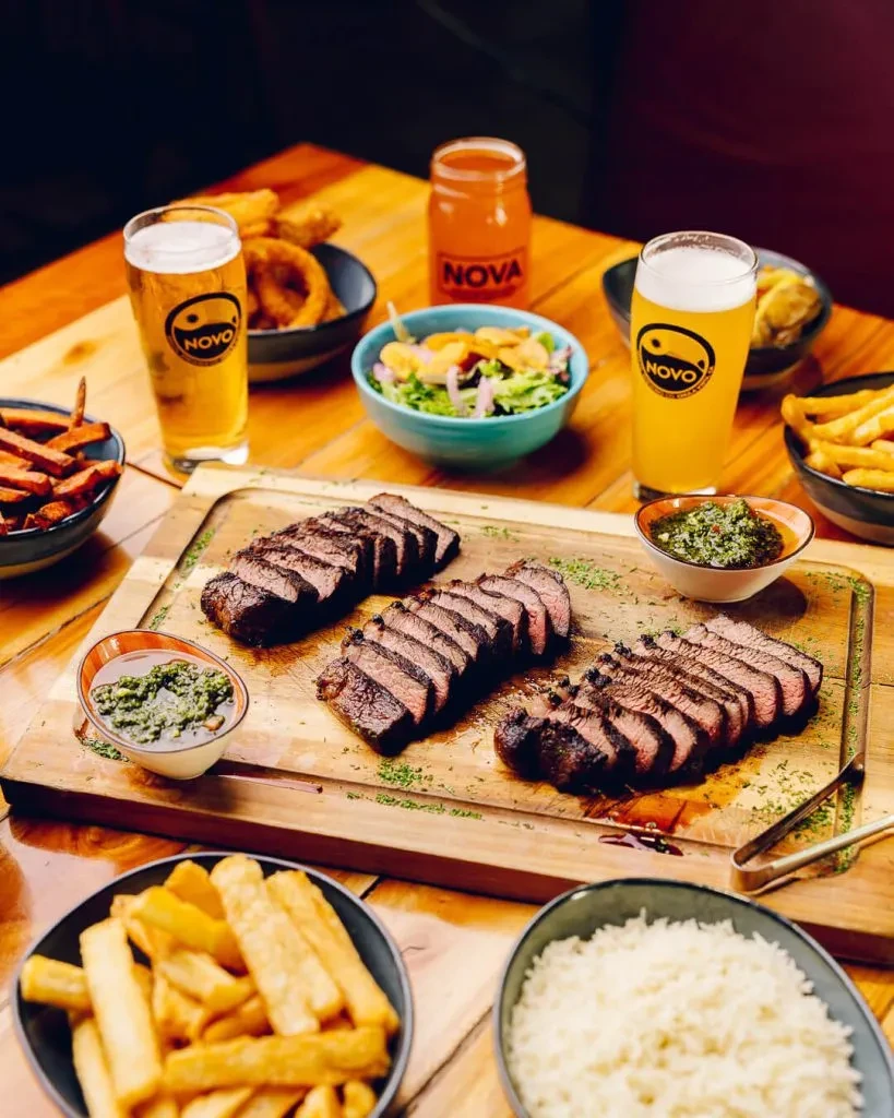 Sliced medium-rare steak, fries, rice, salad, and beer on a wooden table.