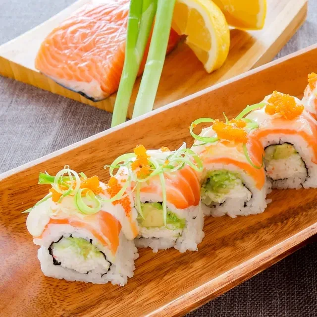 Salmon sushi rolls with tobiko and green onions on wooden platter.