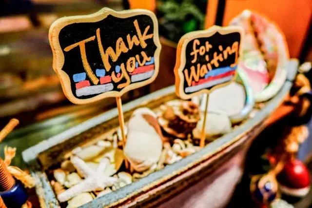 Two chalkboard signs in a boat with seashells read "Thank you for Waiting."