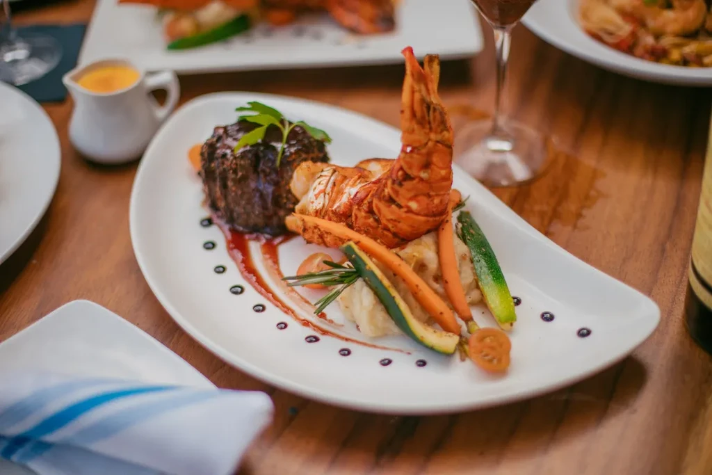 Plated surf and turf: seared steak, grilled lobster, vegetables, sauce.