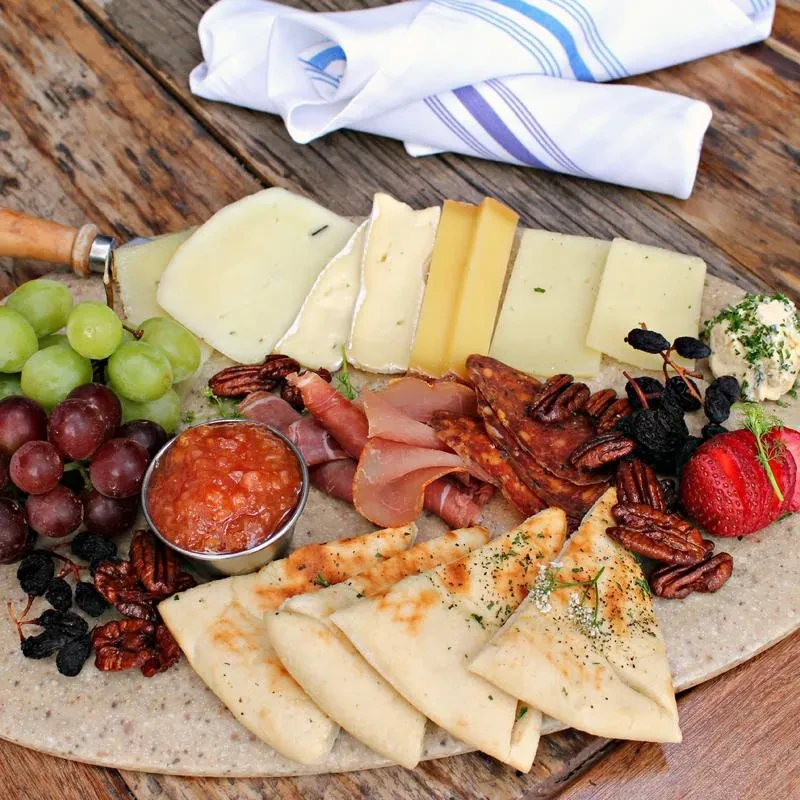 A charcuterie board with cheeses, meats, fruits, nuts, and flatbread.