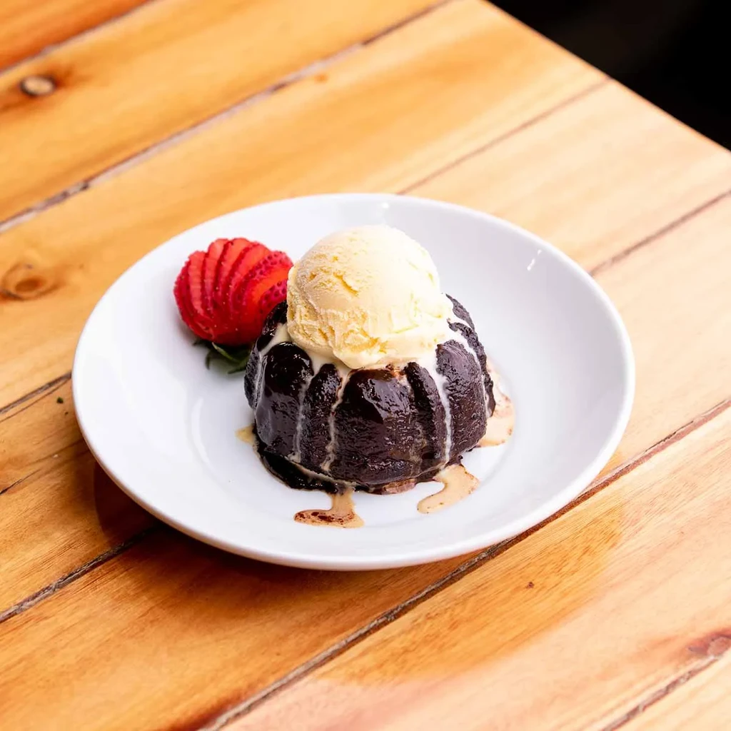 Chocolate cake with melting ice cream, fanned strawberry, and green sprig.