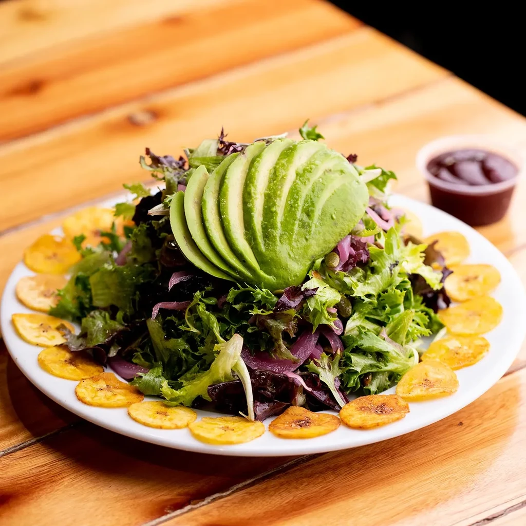 Vibrant green salad with fanned avocado, plantain chips, and sauce.