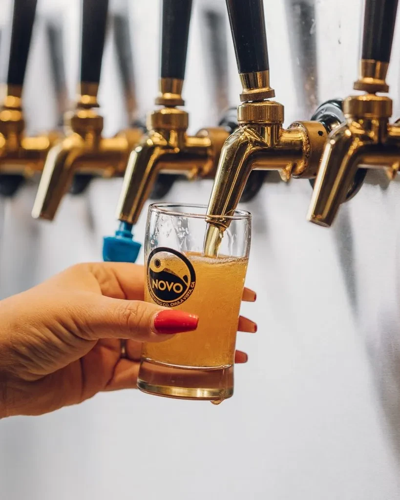 Red-nailed hand fills a NOVO Brewing Co. glass from a brass tap.